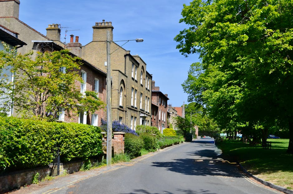 A tall black metal street lamp with a lit lantern at the top stands in front of leafless trees on a foggy day, with multiple directional signs attached to the post. The signs display destinations such as 'Richmond Lock,' 'Isleworth via Lock,' and 'Kew Gardens 1/4m,' indicating nearby locations and walking distances. In the background, there is a brick fence and a small white building with a pitched roof, partially obscured by the fog. The scene is typical of a residential or park area in Dulwich, with an overcast atmosphere. Movable boxes, packing blankets, or moving equipment are not visible in this image, but the setting suggests an environment where house removals and furniture transport may take place. The image is suitable for describing the logistical aspects of home relocation and local moving services in the SE21 Dulwich area, as provided by Movers Dulwich, with a focus on outdoor signage and street scene context.